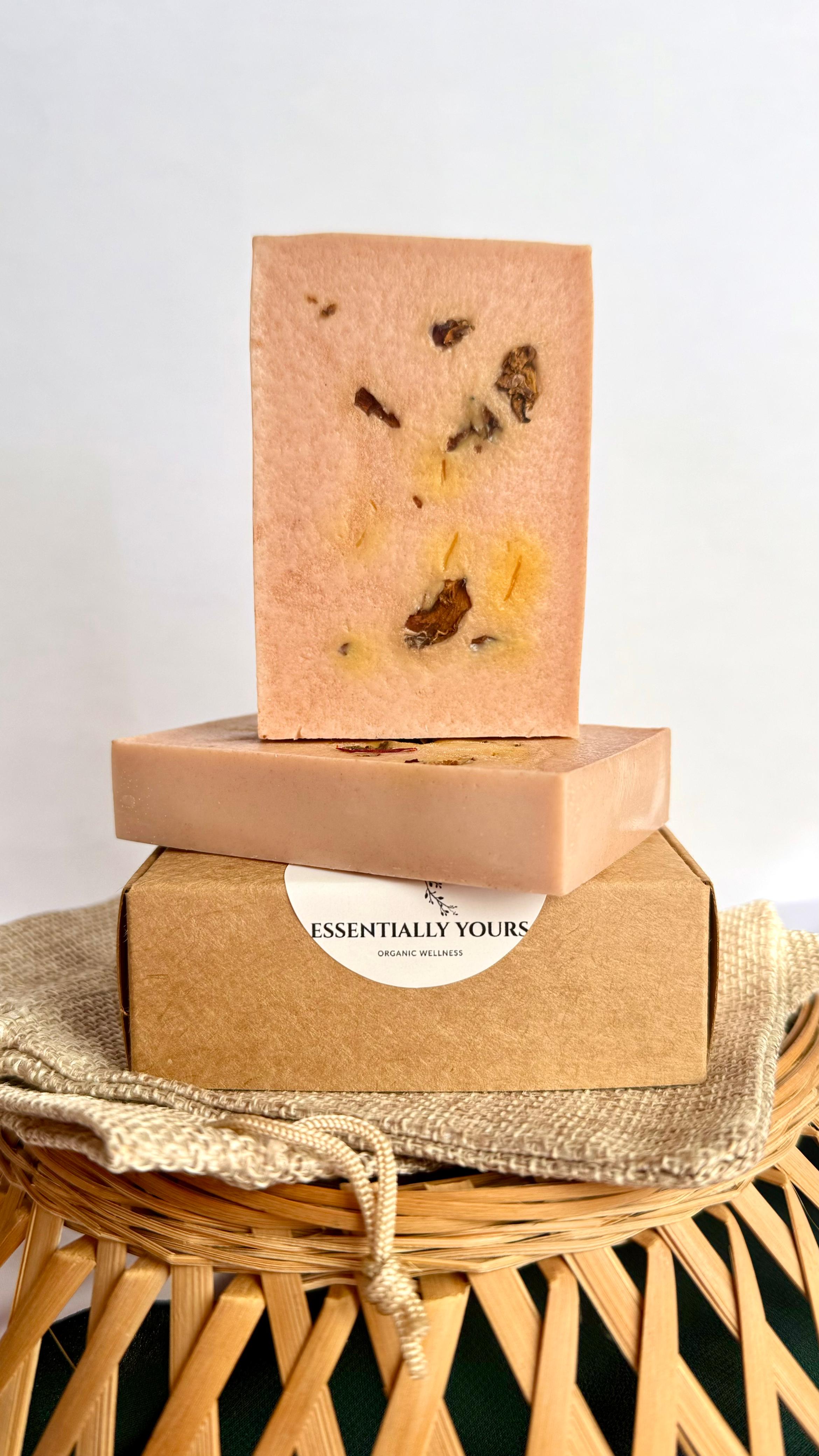 Soft pink and golden handcrafted Wild Rose & Saffron Soap displayed with dried rose petals and saffron strands on a natural textured background, showcasing a luxurious botanical skincare product made with natural ingredients.